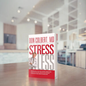 Dr. Colbert’s Stress Less hardcover book by Dr. Don Colbert, MD from Divine Health displayed upright on a modern desk with a soft office background. The wellness book focuses on managing stress, understanding cortisol and stress hormones, and supporting emotional and physical health. It highlights how stress can impact gut health, digestion, and overall wellness while emphasizing healthy habits and nutrition strategies that may include probiotics, fiber supplements, and collagen-supporting foods.