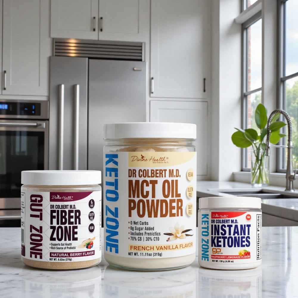 Divine Health Dr. Don Colbert, MD Keto Zone Maintenance Pack arranged on a polished kitchen countertop, featuring three products: Fiber Zone in a maroon-and-white container, MCT Oil Powder in a large beige-and-white jar with blue Keto Zone branding, and Instant Ketones in a small white container with blue and red label accents; all set against a modern kitchen backdrop with stainless-steel appliances, window lighting, and greenery.