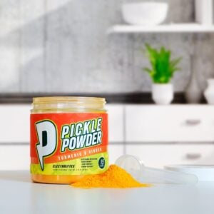 Divine Health Pickle Powder by Dr. Colbert on a kitchen counter with a scoop and bright orange powder supports hydration joint health and muscle recovery with electrolytes and antioxidant ingredients