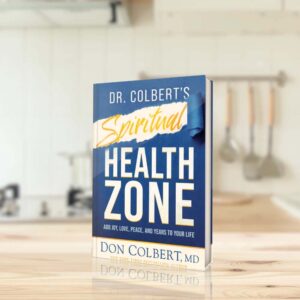 Dr. Colbert’s Spiritual Health Zone hardcover book by Dr. Don Colbert, MD from Divine Health displayed upright on a wooden kitchen countertop with a soft, neutral kitchen background. The book focuses on spiritual wellness and the connection between faith, emotional health, and physical well-being, emphasizing how spiritual balance can support stress reduction, gut health, digestion, and overall wellness alongside healthy lifestyle habits and nutrition.