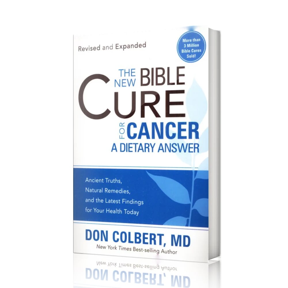 A softcover paperback book titled “The New Bible Cure for Cancer: A Dietary Answer” by Don Colbert, MD is shown standing upright against a clean white background. The book is photographed at a slight angle, allowing the thickness of the softcover spine to be visible along the right side. The cover features a white and blue color scheme with modern typography, a blue circular badge near the top indicating sales information, and subtle leaf graphics across the lower half of the design. The book’s reflection is faintly visible beneath it, creating a polished studio-style presentation.