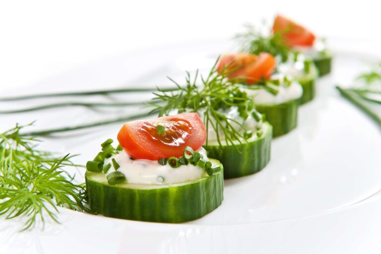 Keto cucumber bites topped with herbed cream cheese, fresh dill and cherry tomato on a serving platter