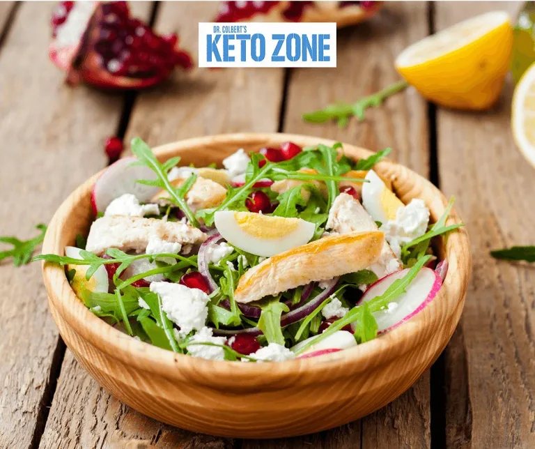 Keto grilled chicken salad with pomegranate seeds, feta and arugula in a white bowl